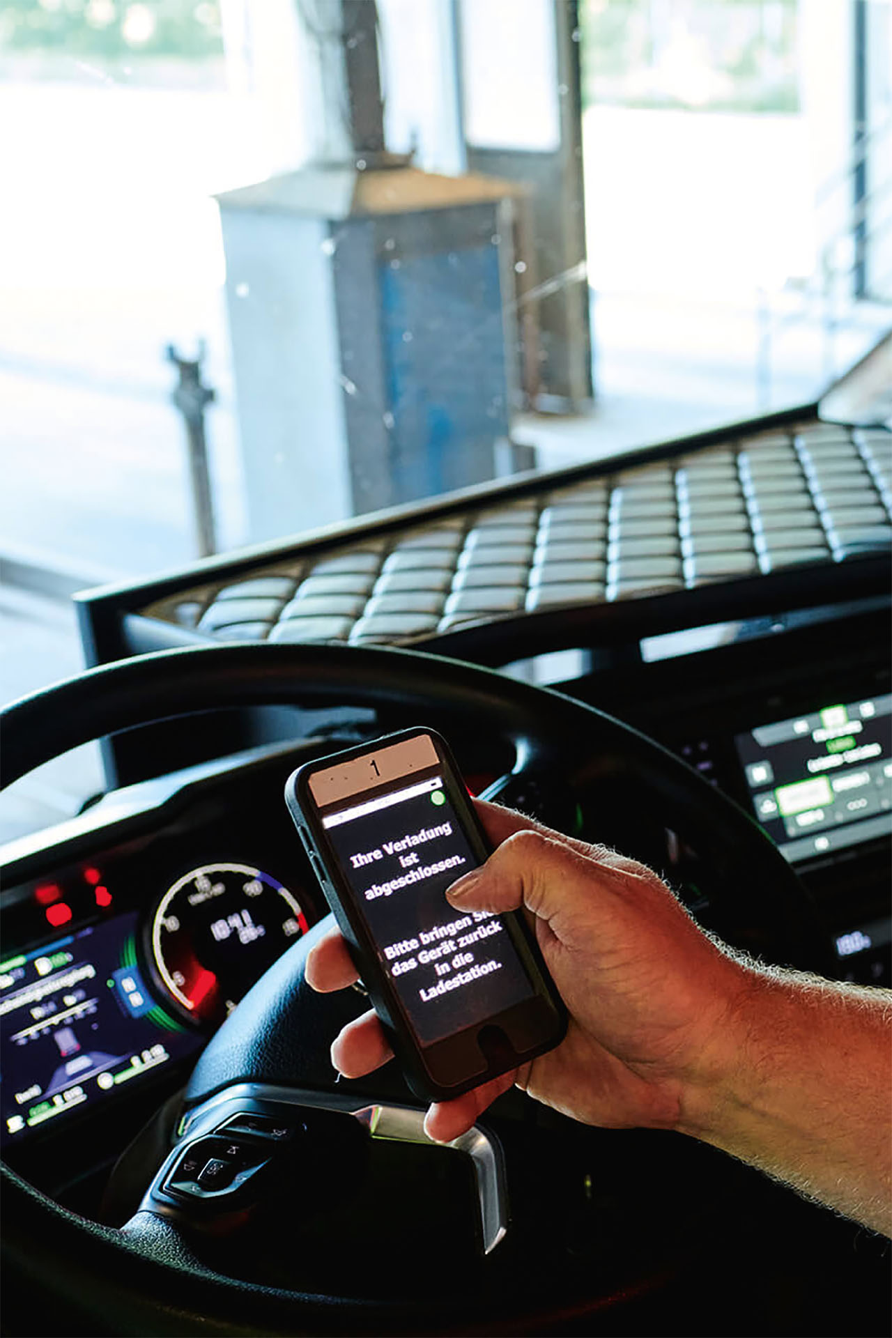 A driver sits in the vehicle and reads a notification on a mobile device that the charging process has been completed.