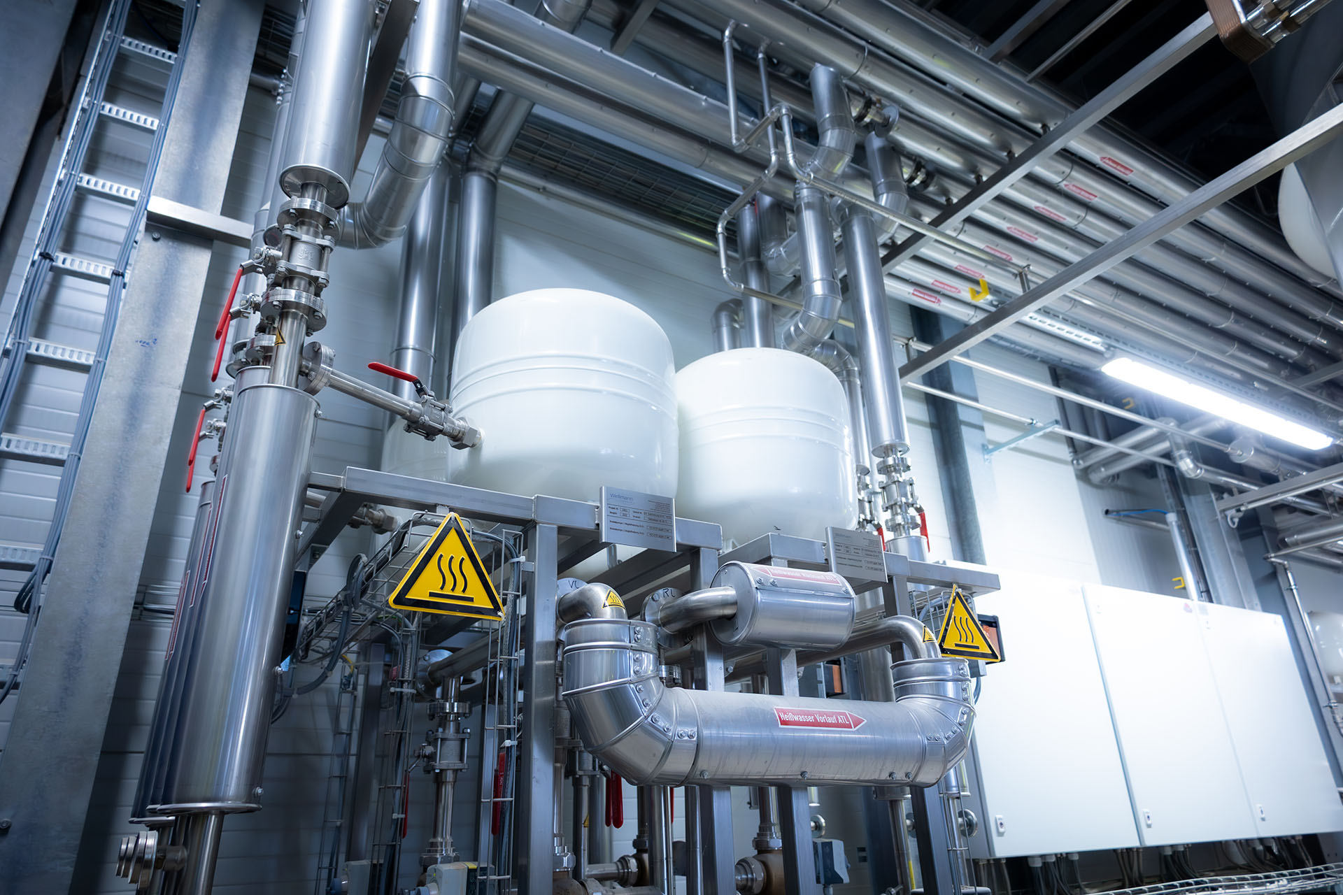 Industrial installation with tanks, pipes and warning signs indoors.