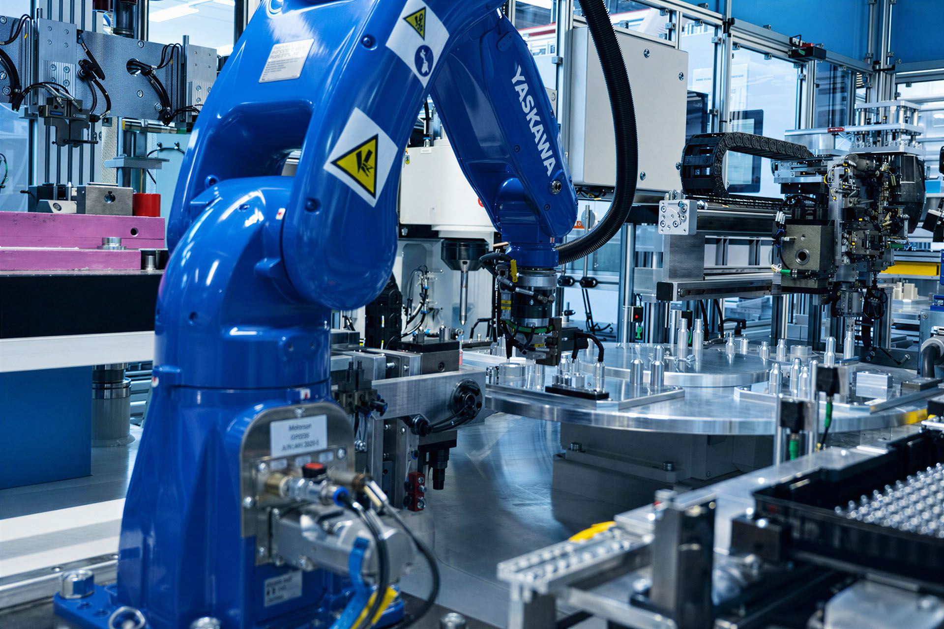 A 6-axis robot loads inserts into a rotary table injection moulding cell.