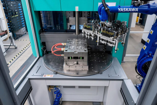 A 6-axis robot positions inserts on a mould mounted on a rotary table.